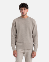 A man wearing a beige RUVR knit pullover with a ribbed crew neck, cuffs, and hem against a grey background.