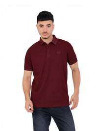 Model wearing a burgundy RUVR Essential Polo shirt in cotton piqué with a tonal embossed chest emblem.