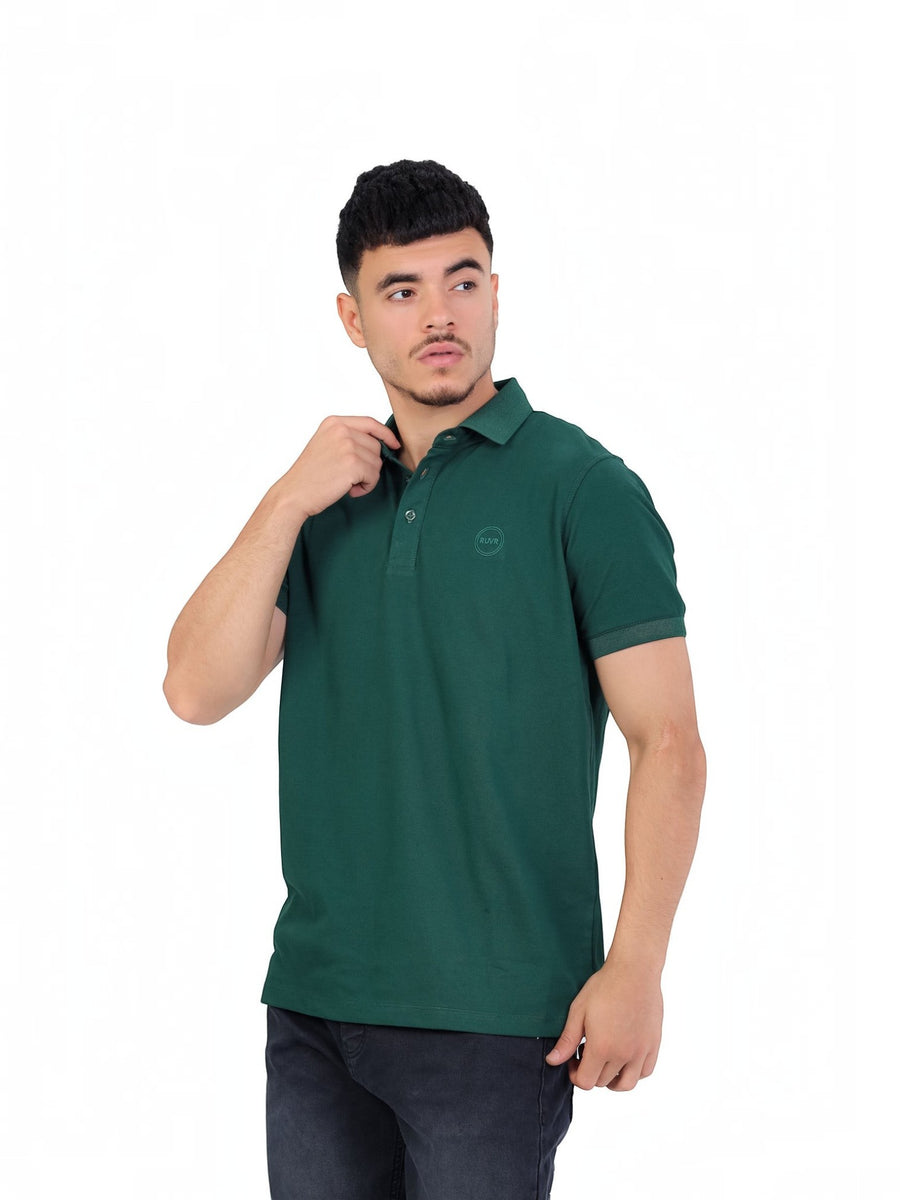 A model wearing a RUVR dark green cotton pique polo shirt with a tonal embossed emblem and three-button placket.