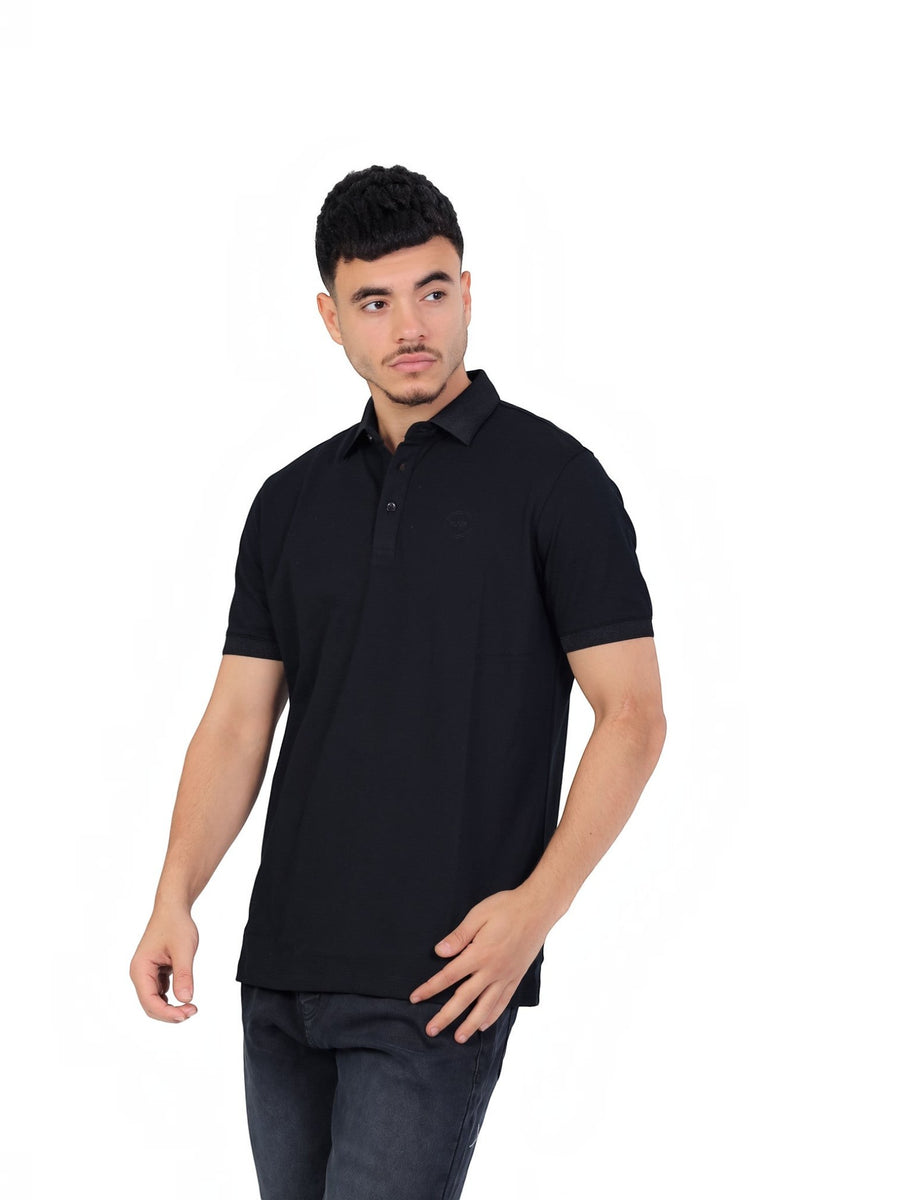 Model wearing a black RUVR Essential Polo shirt in 100% cotton piqué with a tonal embossed emblem and ribbed collar.