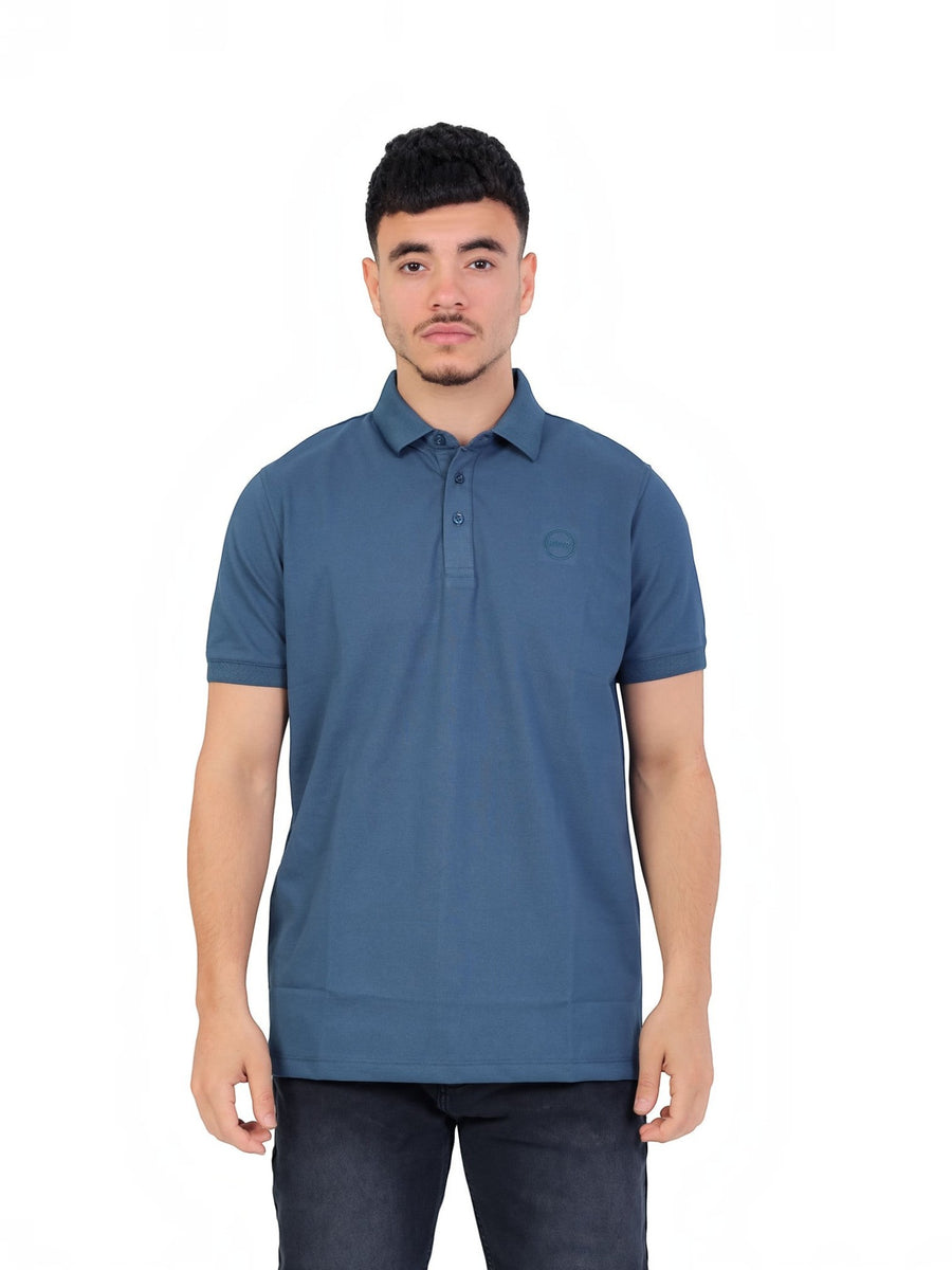 A model wearing a blue RUVR Essential Polo shirt in cotton piqué with a tonal embossed emblem and three-button placket.