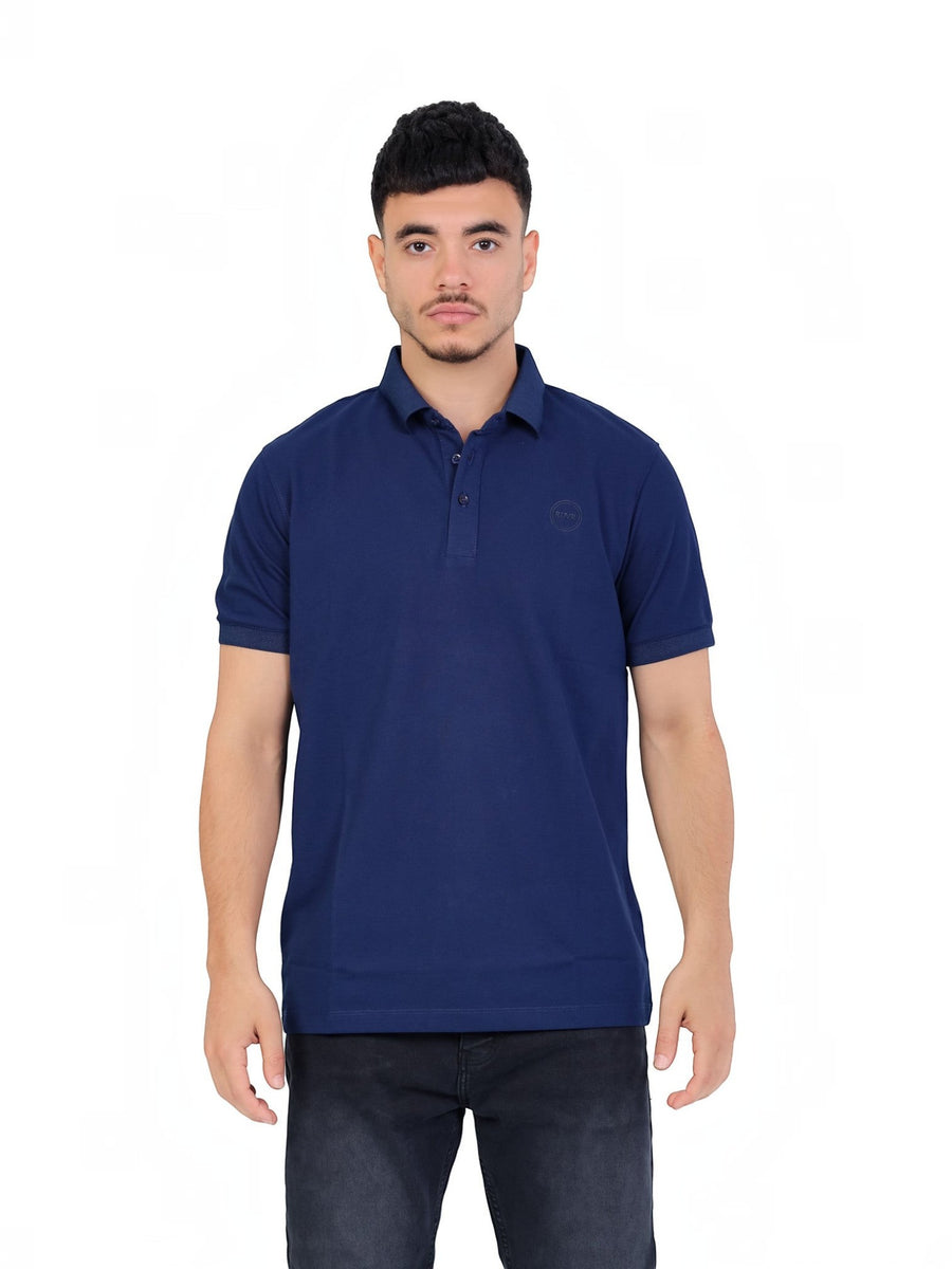 A model wearing a navy blue RUVR Essential Polo shirt in cotton piqué with a tonal embossed chest emblem.