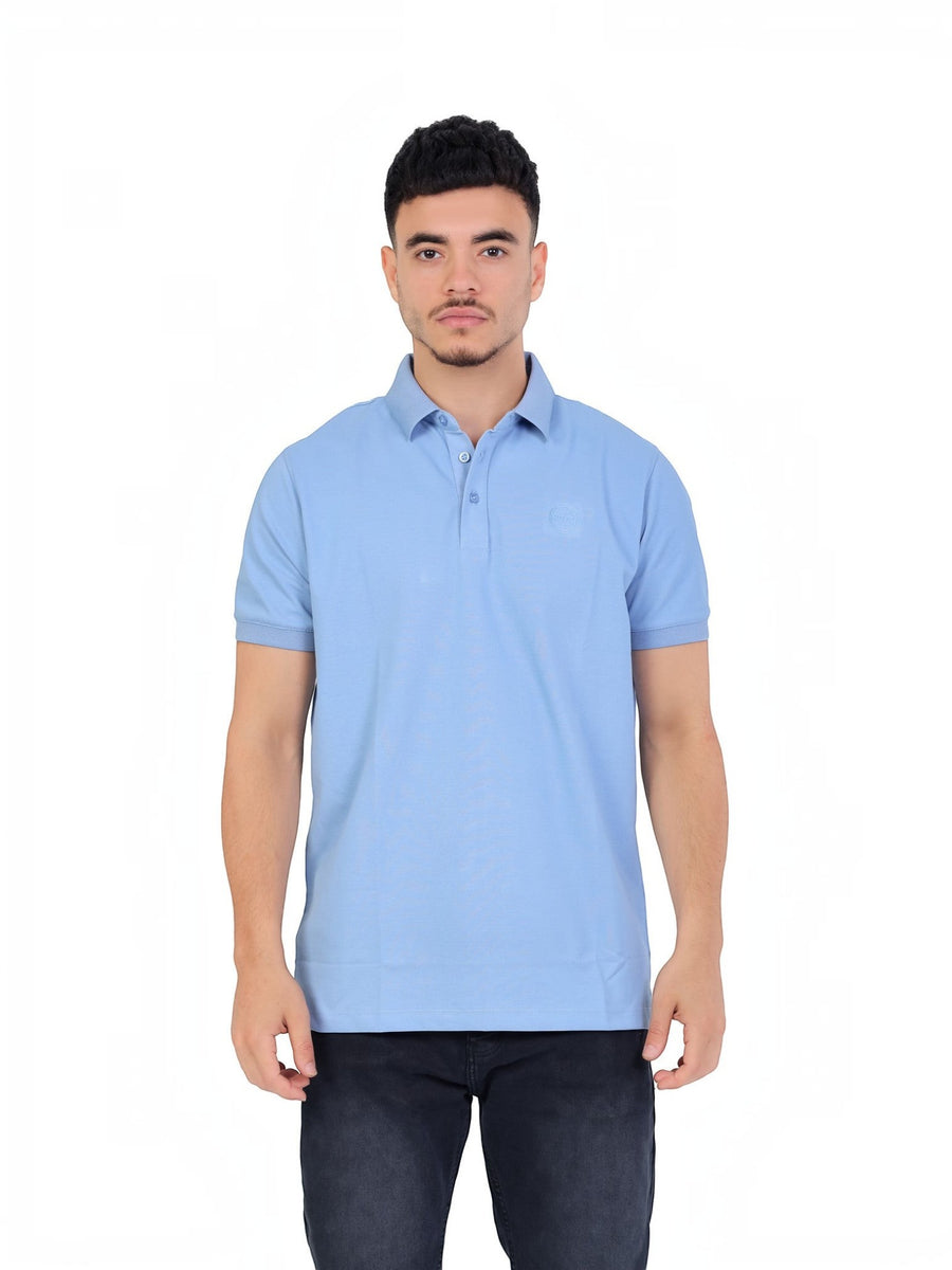 A model wearing a light blue RUVR Essential Polo shirt in cotton piqué with a tonal embossed emblem and ribbed cuffs.
