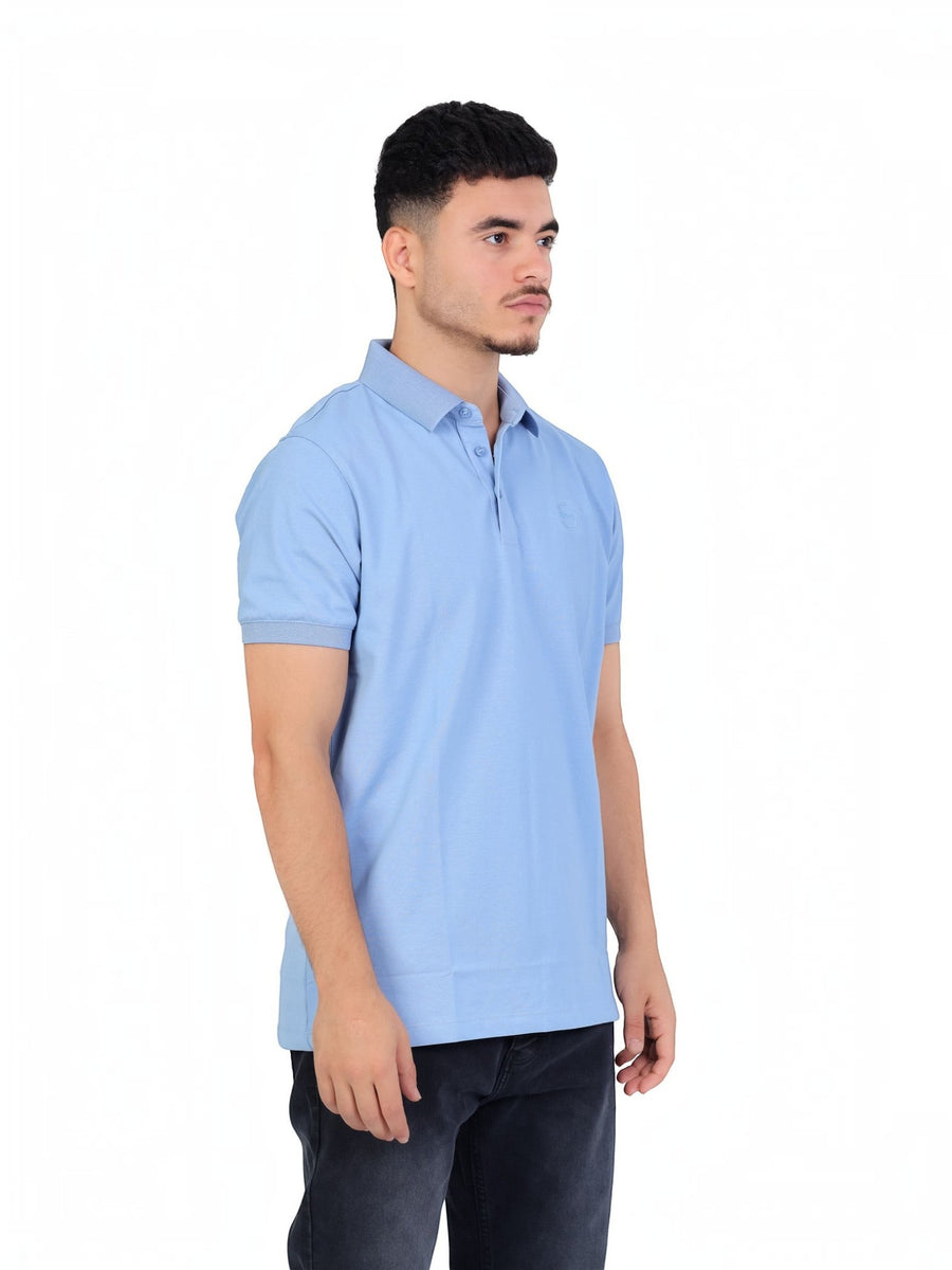 A model wearing a light blue RUVR Essential Polo shirt in cotton piqué with a tonal embossed emblem and ribbed cuffs.