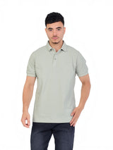 A model wearing a sage green RUVR Essential Polo shirt in cotton piqué with a tonal embossed chest emblem.