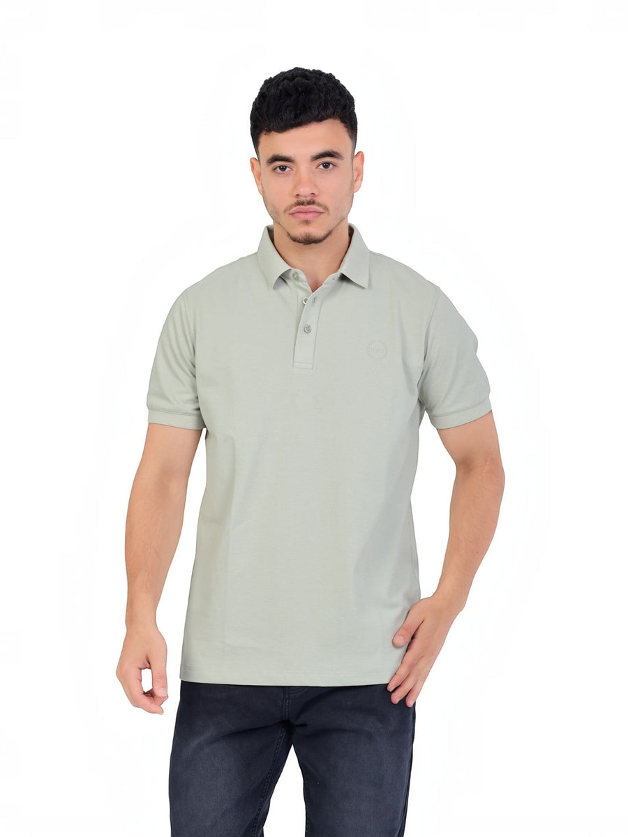 A model wearing a sage green RUVR Essential Polo shirt in cotton piqué with a tonal embossed chest emblem.
